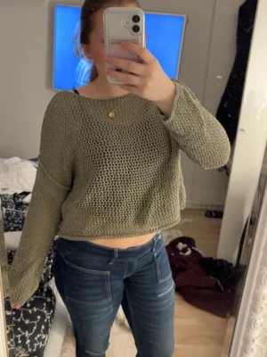 Olivgrön stickad croppad tröja Pull&Bear - Säljer en olivgrön croppad stickad tröja från Pull&Bear. Tröjan har ett grovmaskigt, luftigt mönster och långa ärmar. Perfekt till jeans och för lager-på-lager-stil. Superbekväm och snygg till vardags.