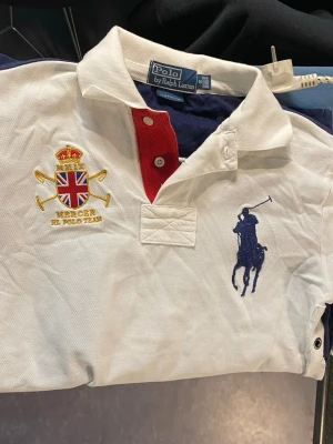 Vit och marinblå Polo Ralph Lauren skjorta - Säljer en klassisk Polo Ralph Lauren skjorta i vit och marinblå med röd knappslå. Stor broderad logga på bröstet, brittiskt inspirerat emblem och stor siffra 3 på ryggen. Skjortan har korta ärmar och är i bomull med custom fit-passform.