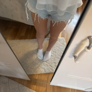 Ljusa jeansshorts med fransar - Säljer ett par ljusa jeansshorts med fransiga kanter. De har en avslappnad passform och är perfekta för sommardagar. Shortsen har en klassisk femficksdesign och knappar framtill.