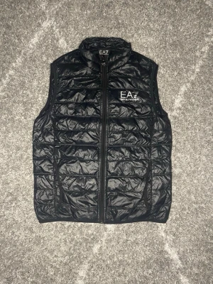 Emporio Armani väst M - Svart väst från EA7 Emporio Armani, storlek M. Lätt och bekväm att ha på sig, med dragkedja och fickor. Passar bra både till vardags och när man vill ha något enkelt men snyggt. I fint skick.