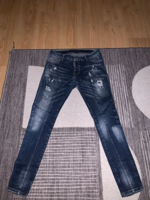 Dsquared2 blå skinny jeans herr - Snygga blå jeans från Dsquared2 med slitna detaljer och skinny passform. Jeansen har coola slitningar och tryck på bakfickan, klassisk femficksmodell och orange kontrastsömmar. Perfekta för dig som gillar streetstyle och vill sticka ut.