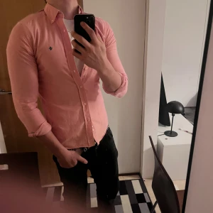 Rosa skjorta från Morris Stockholm S - Säljer en snygg rosa skjorta från Morris Stockholm i storlek S (37/38). Skjortan har klassisk krage, knappar framtill och en broderad logga på bröstet. Tillverkad i bomull med Twofold Yarn för extra komfort och stil.