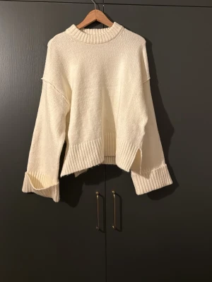 Vit oversized stickad tröja - Mysig vit stickad tröja med oversized passform och breda ribbade muddar vid ärmslut och nederkant. Tröjan har lång ärm och hög, ribbad halsringning. Tröjan är från Gina tricot och har inte använt en enda gång!
