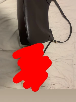 Svart axelväska i skinn - Snygg svart axelväska i slätt skinn med minimalistisk design och guldfärgade metalldetaljer. Väskan har en justerbar axelrem och dragkedja upptill. Perfekt storlek för att få plats med allt du behöver till vardagen.