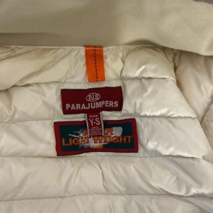 Beige lättviktsdunjacka Parajumpers - Säljer en superlätt beige dunjacka från Parajumpers med dragkedja framtill och klassisk logga på ärmen. Jackan har quiltad design, hög krage och smal passform. Perfekt för dig som vill ha en stilren och bekväm jacka till vardags.