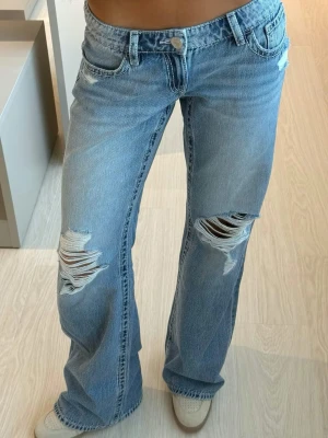 Blå bootcut jeans med slitningar - Säljer ett par ljusblå lågmidjade bootcut jeans från Gina Tricot med snygga slitningar över knäna och klassiska fem fickor. En julklapp som tyvärr inte passade💕