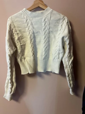 Vit stickad tröja från Stay - Säljer en vit stickad tröja från Stay med grova flätstickade detaljer på både ärmar och framstycke. Tröjan har ribbade muddar och midja, samt lång ärm. Perfekt för dig som gillar en mysig och trendig look.