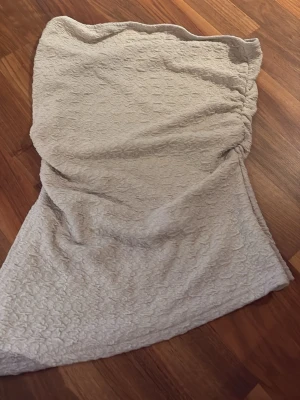 Beige topp med strukturmönster - Säljer en beige topp med snygg struktur i tyget och lätt volang. toppen har en diskret drapering på sidan och är fodrad för extra komfort. Perfekt för dig som gillar en stilren men ändå unik look.