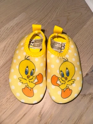 Gula prickiga barnskor med Tweety LC Waikiki Tofflor Gul EUR 19-20 - Supersöta gula barnskor med vita prickar och Tweety-tryck framtill. Skorna har elastisk öppning med gul kant och en liten ögla bak. Ovandelen är i mjuk textil och sulan är svart och mönstrad för bra grepp. Perfekta för små fötter som vill sticka ut!Söta gula tofflor med prickar och motiv. Perfekt för små fötter.