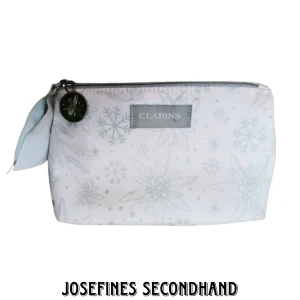 Blommig vit necessär - Supersöt necessär i vitt från Clarins. Med rosett, blommor och snöflingor som mönster. Är i använt skick