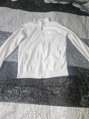 Vit zip hoodie från Nike M - Säljer en clean vit hoodie från Nike i storlek M. Tröjan har dragkedja framtill, två fickor och klassisk Nike-logga på bröstet. Tillverkad i mjuk polyester med lång ärm och ribbade muddar. Perfekt för träning eller chill dagar.