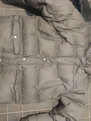  Äkta dunjacka från Boomerang - Säljer en grå, klassisk dunjacka från Boomerang i storlek M. Jackan har stora fickor med tryckknappar och en puffig, quiltad design som håller dig varm under kalla dagar. Perfekt för dig som vill ha en stilren och funktionell vinterjacka. Mindre slitage finns, därav lågt pris. Varm och bekväm jacka. Skick: Använt (2 vintrar) Nypris: 6999:-