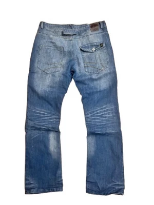 Blå jeans bootcut från Stanwick, storlek 36/32 - Säljer ett par blå jeans från Stanwick med bootcut ben och coola kontrastsömmar i gult och brunt. Jeansen har klassiska fem fickor, en bakficka med lock och knapp samt detaljerad logga på bakfickan. Perfekta för dig som gillar en avslappnad och tidlös look.