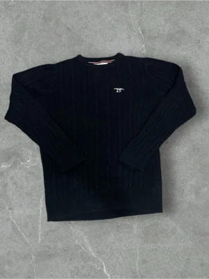 Mörkblå kabelstickad tröja Hampton Republic - Säljer en mörkblå kabelstickad tröja från Hampton Republic med broderad logga och siffran 27 på bröstet. Tröjan har rund halsringning och långa ärmar. Perfekt för dig som gillar klassisk och stilren look.