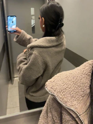 Beige teddyjacka  - Mysig beige teddyjacka med dragkedja framtill och stor krage. Jackan har en loose passform och är tillverkad i fluffigt teddy-material som håller dig varm. Perfekt för dig som gillar en avslappnad och trendig stil.