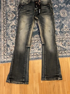 Bootcut jeans från Purple Brand - Bootcut jeans från Purple Brand i tvättad blå denim med slitningar och ljusa partier. Klassisk femficksmodell med låg midja och förstärkta benslut. Snygg kontrastsöm och cool vintagekänsla. Perfekta för dig som gillar en avslappnad men trendig look.