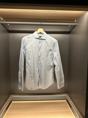 Ljusblå Riley skjorta med mönster - Säljer en ljusblå skjorta från Riley med små cirkelmönster och regular fit. Skjortan har klassisk krage, långa ärmar och knappar framtill. Perfekt för dig som gillar stilrena detaljer och vill ha en skjorta som sticker ut lite extra.