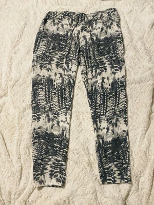 Mönstrade byxor från Vero Moda XL - Säljer ett par snygga byxor från Vero Moda i storlek XL. Byxorna har svartvitt abstrakt mönster, dragsko i midjan och raka ben. De är tillverkade i ett mjukt och lätt material som känns skönt mot huden. Perfekta för dig som gillar statement-plagg!