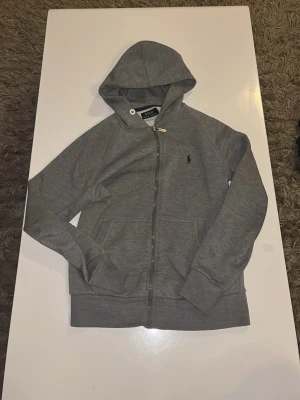 Grå zip hoodie Ralph lauren - Säljer nu denna feta Ralph lauren zip. Säljer den för jag har växt ur den. Inga skador och skicket är väldigt bra. Skulle säga att den passar folk runt 165-170cm långa. Skriv vid minsta fråga och priset är inte hugget i sten!