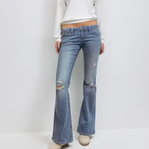 Blå bootcut jeans med paljettdetalj - Snygga ljusblå bootcut jeans med slitningar och paljettdetaljer på bakfickan. Jeansen har låg midja. Innerbenslängd: 87 cm