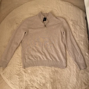 Bondelid QuarterZip - Snygg beige stickad tröja från Bondelid med half zip och ribbade muddar. Klassisk och stilren modell med hög krage och diskret broderad logga på bröstet. Perfekt för lager-på-lager och passar till allt. Supermjuk och skön att ha på sig.