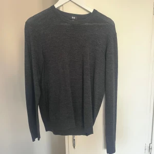 Mörkgrå stickad tröja från Uniqlo - En stilren mörkgrå stickad tröja från Uniqlo i storlek S. Tröjan har rund halsringning och långa ärmar, perfekt för lager-på-lager. Enkel och clean design som funkar till allt. Materialet är mjukt och skönt, passar dig som gillar minimalistisk stil.