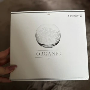 Orrefors Organic Vase - Elegant Orrefors Organic vas i originalförpackning. Glasvas med vackert trädmotiv, perfekt för blommor eller som inredningsdetalj. Produkten är oanvänd förpackningen har ett litet märke på ovansidan men är annars i gott skick.