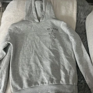 Grå hoodie med tryck 'Ma Chérie' - Säljer en ljusgrå hoodie med svart tryck 'Ma Chérie' och en stjärna både fram och bak. Tröjan har huva, långa ärmar och ribbade muddar vid ärmslut och nederkant. Perfekt för sig som exempelvis gillar Hov1💕STORLEK 146/152. Lite knott o sånt men annars i bra skick! Nästan aldrig använt❣️Saknar snören.
