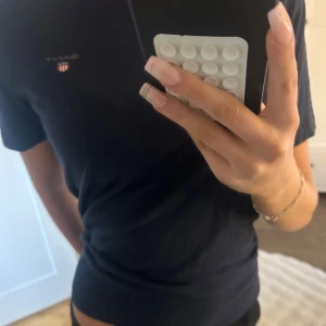 Mörkblå t-shirt från GANT - Snygg mörkblå t-shirt från GANT med diskret logga och liten sköld på bröstet. Klassisk rund hals och korta ärmar. Tillverkad i mjuk bomull som känns skön mot huden. Perfekt basic-plagg med stilren look och normal passform.