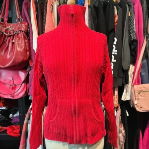 Röd stickad polotröja  - Riktigt snygg röd stickad polotröja med hög krage och kabelstickat mönster. Tröjan har långa ärmar, ribbade muddar och ficka framtill. 