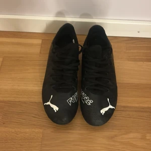  Puma fotbollsskor  - Svarta Puma Future fotbollsskor med vit logga och snörning. Skorna har rund tå och platt sula med dobbar för bra grepp på planen. Tillverkade i syntetmaterial. (Utesko) pris kan diskuteras!