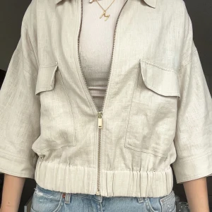 Beige overshirt med dragkedja - Snygg beige overshirt med dragkedja framtill, två stora bröstfickor med lock och resår i midjan. Jackan har trekvartsärmar och är tillverkad i ett lätt linneliknande material. Perfekt för lager-på-lager och chill stil. som ny, köpt i augusti och aldrig använts. därför i väldigt bra skick. 