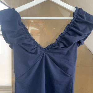 Marinblå top Holly & Whyte S - Supersöt marinblå fest top från Holly & Whyte by Lindex i storlek S. Toppen har en snygg v-ringning med rynkade detaljer längs axlarna och är tillverkad i ett mjukt bomullstyg. Perfekt för dig som gillar en enkel men stilren look.