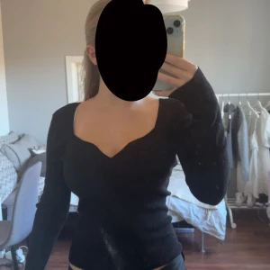 Svart stickad tröja med v-ringning - Snygg svart stickad tröja med unik v-ringad hals och långärmade ärmar. Modellen är figurnära och har en cool, lite vågig kant vid halsen som ger extra stilpoäng. Perfekt för dig som gillar enkla men trendiga plagg.