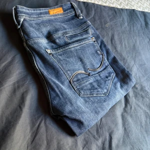 Jack and Jones jeans  - Säljer ett par blå Jack and Jones jeans med klassisk femficksdesign och snygga detaljer på bakfickorna. Jeansen har en slim passform och är tillverkade i mjukt denimtyg med lätt tvättad look. Perfekta för dig som gillar stilrena och bekväma jeans.