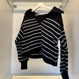 Svartvit randig stickad tröja med krage - Säljer en svart stickad tröja med vita ränder och bred krage. Tröjan har v-ringning framtill, långa ärmar och ribbade muddar. Perfekt för dig som gillar en chill och trendig look med lite oversized känsla.