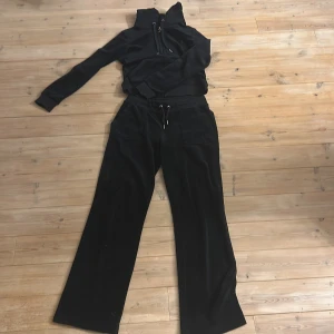 Svarta mjukisbyxor i velour med snörning - Svarta mjukisbyxor från Juicy Couture i mjuk velour med breda ben och dragsko i midjan. Byxorna har stora fickor framtill och en diskret JC-logga på ena fickan. Perfekta för en chill och avslappnad look, byxorna har även pickor på bakdelen.