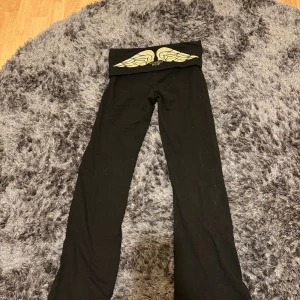 Svarta yogapants Victoria's Secret - Svarta yogapants från Victoria's Secret med guldglittrande vingar och logga på den vikbara midjan. Byxorna har en tight passform upptill och lätt utsvängda ben. Mjukt bomullsmaterial som är skönt mot huden. 💗