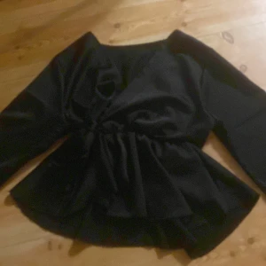 Svart omlottopp med knyt i midjan från missay!! Xs/s! - Från missay!! Säljer en svart omlottopp med långa ärmar och snygg knytning i midjan. Toppen har en v-ringad design och ett lätt glansigt tyg som ger en elegant look. Passformen är normal och den har en volangliknande nederdel som ger extra stilpoäng.