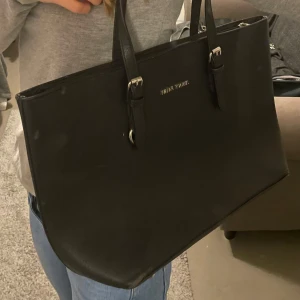 Jenny fairy väska svart läder med ficka stor - Rymlig stor väska som passar perfekt till skolan/jobbet. Dator, böcker samt annat man vill ha med sig får plats. Sitter perfekt och har sköna band. Defekter på bottnen av väskan på alla hörn som man kan se ovan. Måtten är ungefär 32 cm x 26 cm x 13 cm