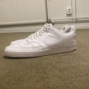 Nike Air Force 1 helvita sneakers - Säljer ett par klassiska helvita Nike Air Force 1 sneakers i skinn. De har perforerade detaljer på tån, rund tå och snörning. Perfekta för dig som gillar en clean och tidlös look. Modellen är low och passar till det mesta.