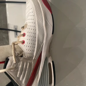 Nike Jordan 1 sneakers vit/röd - Säljer ett par Nike Jordan 1 sneakers i vit och röd med svarta detaljer. Skorna har perforerad ovandel i skinn, mesh på plösen och snörning med röda öljetter. Snygg Jumpman-logga på plösen och hälen, samt grå sula med platt profil. Perfekt för dig som gillar streetstyle.