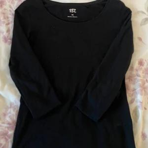 Långärmad topp - En basic svart långärmad topp från 157 i storlek XS. Tillverkad i mjuk bomull med lite stretch för en bekväm passform. Enkel och stilren design med rund halsringning. Perfekt att matcha med vad som helst.  !Armarna är uppvikta på bilden!