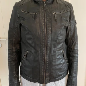 Svart skinnjacka med dragkedjor - Snygg svart skinnjacka med coola detaljer som flera dragkedjor framtill och på ärmarna. Jackan har markerade sömmar, ståkrage  och figurnära passform. Stl 42 men upplever den som 40. Snyggt sliten