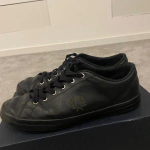Fred Perry - Säljer ett par svarta sneakers från Fred Perry som nypris ligger på cirka 1700kr. Klassisk Fred Perry-logga i mörkgrönt på sidan. Tillverkade i mjukt skinn för en clean och stilren look. Box ingår med köp. Kontakta gärna vid frågor osv. Pris kan diskuteras.