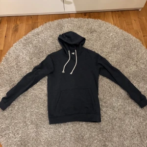 Mörkblå hoodie från Pier One - Säljer en stilren mörkblå hoodie från Pier One med vit snörning i huvan och en stor magficka. Perfekt för dig som gillar en enkel och clean look. Långärmad och i mjukt material som känns skönt mot huden.