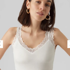Vit spetskantad linnetopp från Vero Moda - Supersöt vit linnetopp med breda axelband i spets och v-ringning. Toppen är figurnära och har en mjuk, stretchig känsla. Perfekt att styla med jeans, kjol eller som detalj under en off-the shoulder topp. Modellen heter VMROSA.