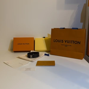 L och V svart armband i skinn - Stilrent svart armband från L och V i äkta skinn med silverfärgat -logo framtill. Armbandet har diskret monogrammönster och justerbart spänne. Kommer med originalask, dustbag och certifikat. Perfekt accessoar för dig som gillar lyxiga detaljer.