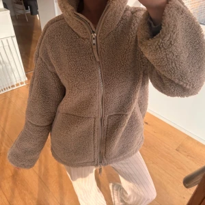 Beige teddyjacka med dragkedja - Mysig beige teddyjacka med hög krage och hel dragkedja framtill. Jackan har två stora fickor och en loose passform som ger en chill vibe. Perfekt för kalla dagar när du vill vara både varm och snygg.
