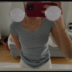 Randig blåvit topp med kort ärm - Säljer en fräsch topp med smala svarta och vita ränder. Modellen har rund hals och korta ärmar, perfekt för en chill och stilren look. Materialet känns mjukt och skönt mot huden, troligtvis bomull. Passar dig som gillar enkel och klassisk stil.